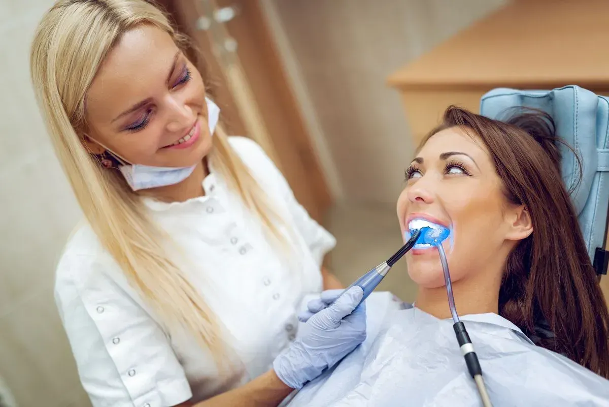 A woman is getting her teeth whitened by a dentist.