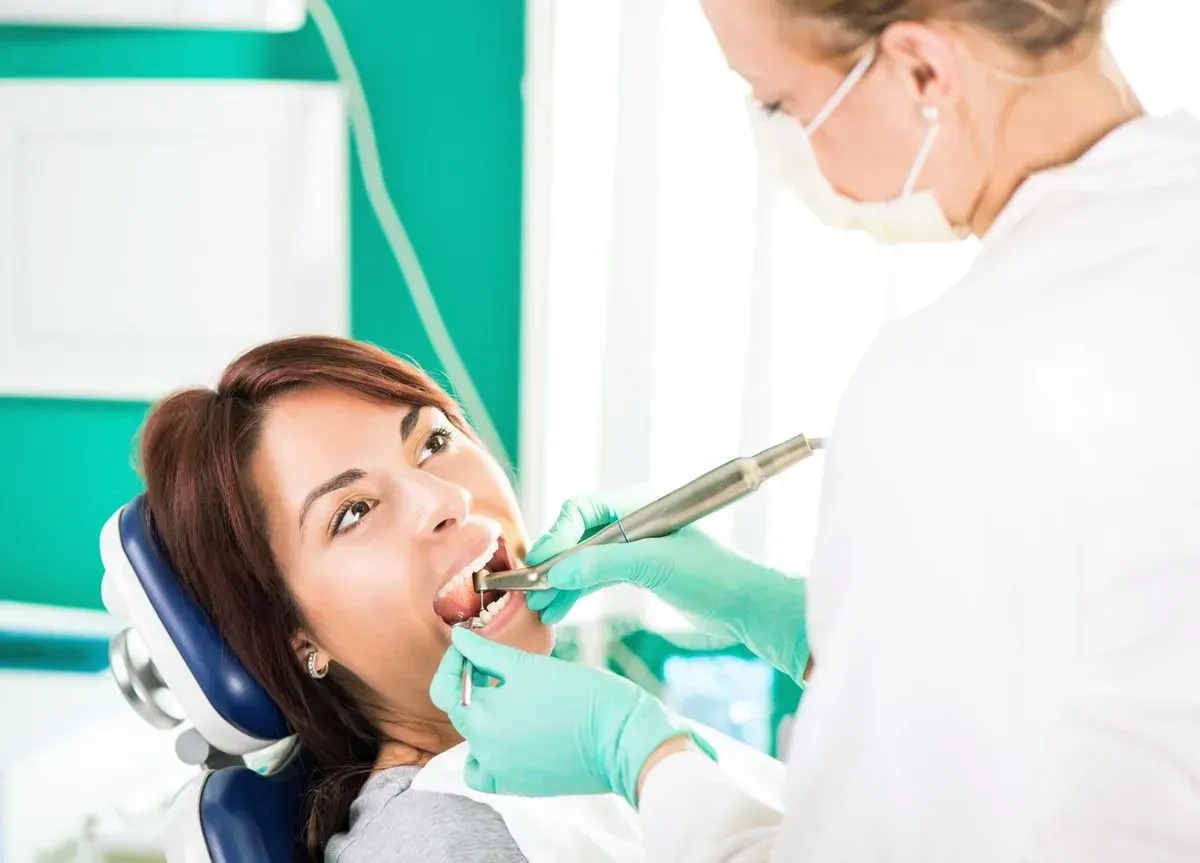 A woman is sitting in a dental chair getting her teeth examined by a dentist.