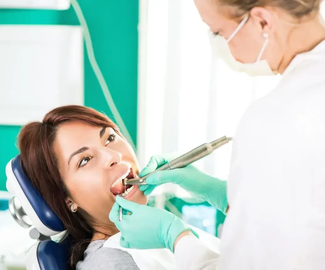 A woman is sitting in a dental chair getting her teeth examined by a dentist.
