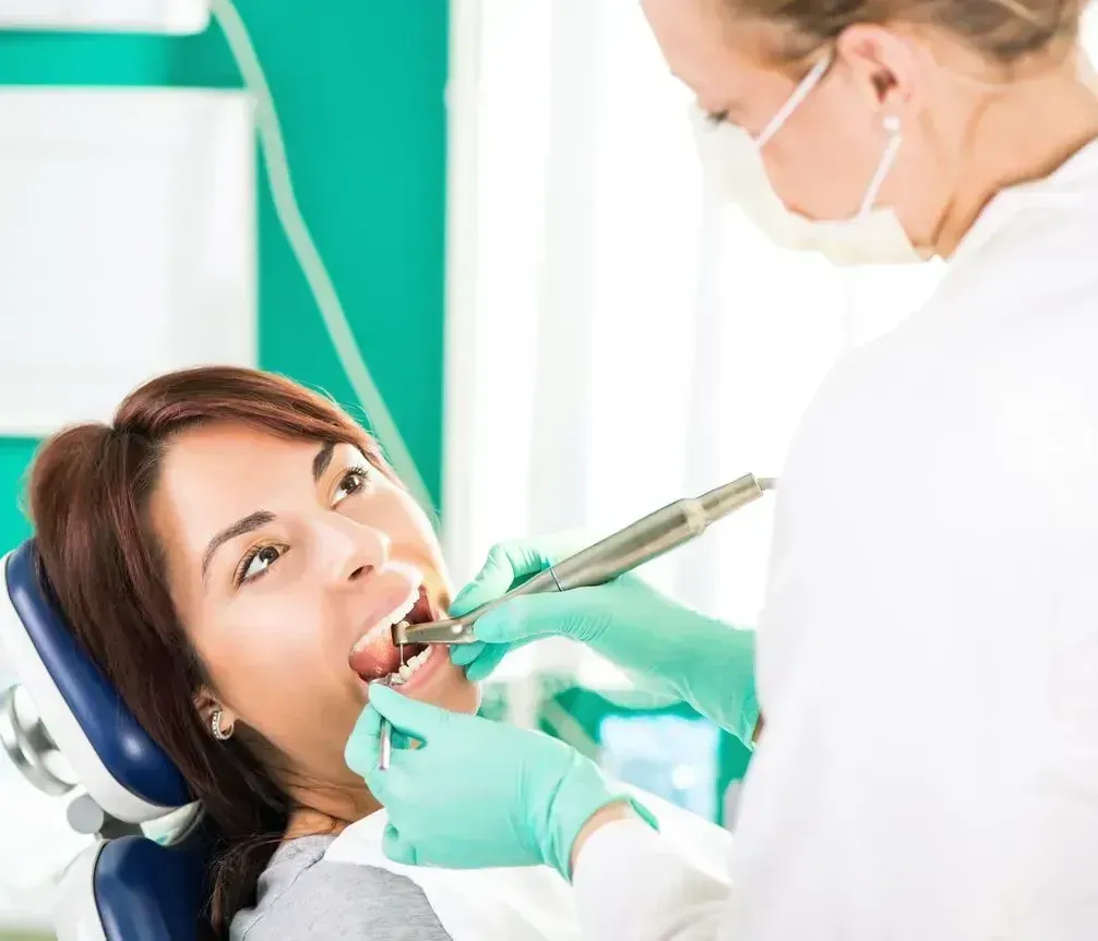 A woman is sitting in a dental chair getting her teeth examined by a dentist.