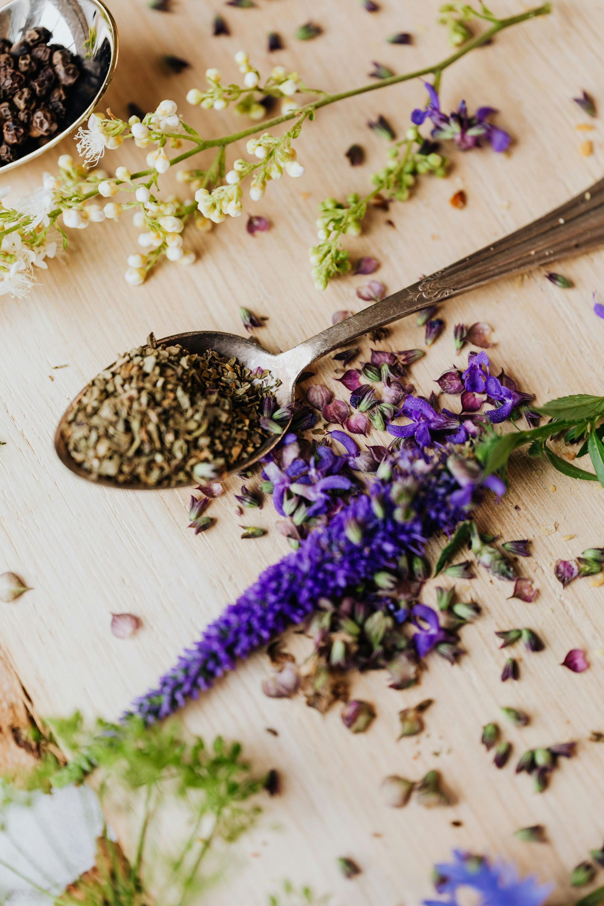 A spoon filled with herbs and flowers on a wooden table.