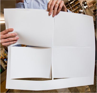 Person holding a large white paper with four sections, likely after cutting.
