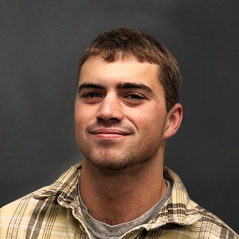 Man in plaid shirt smiles slightly against a gray background.