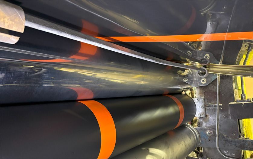Close-up of industrial machinery with black and orange cylinders, metal supports, and a reflective surface.