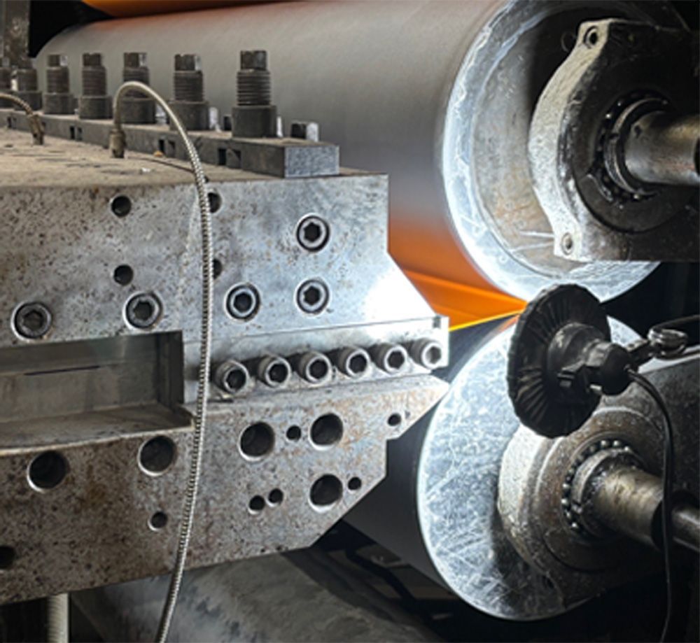 Industrial machine processing orange paper between large rollers.