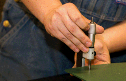 Person using a precision measuring tool on a green surface. Hands are holding the tool.