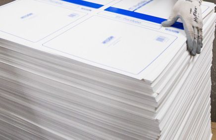 Stack of white paper sheets with blue printed details, hand in a glove holding a sheet.