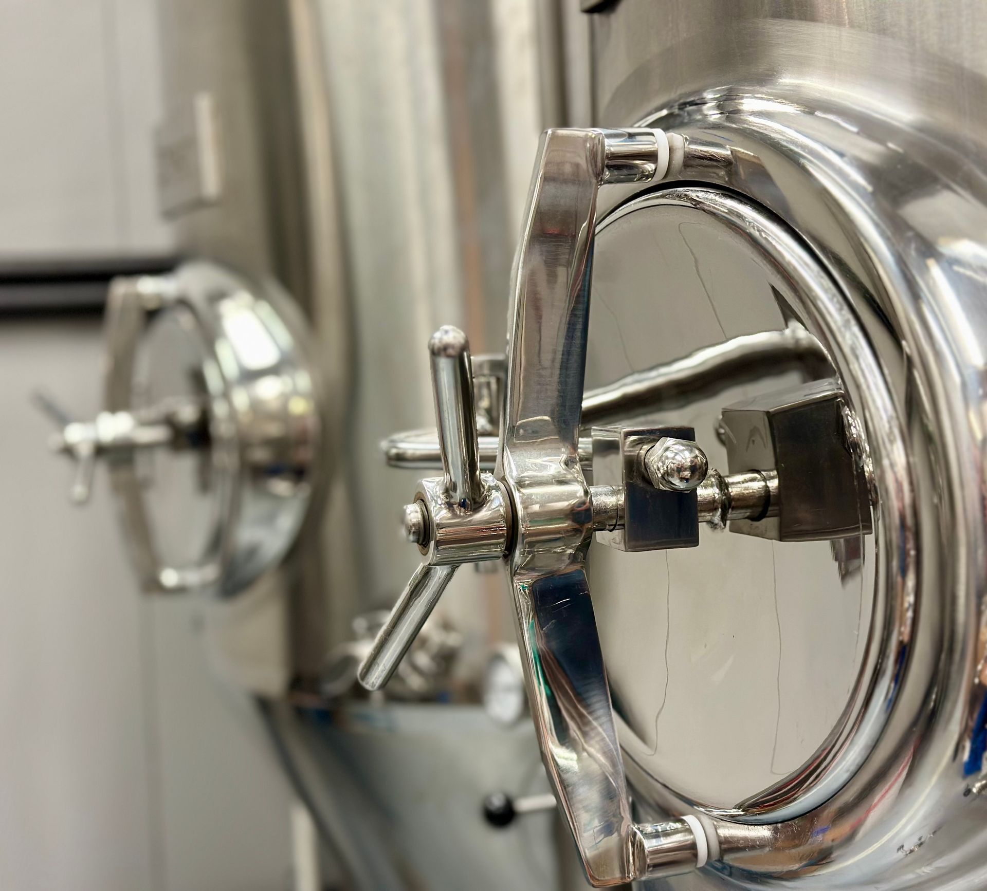 Stainless steel industrial tank with a circular door, handle, and latches.