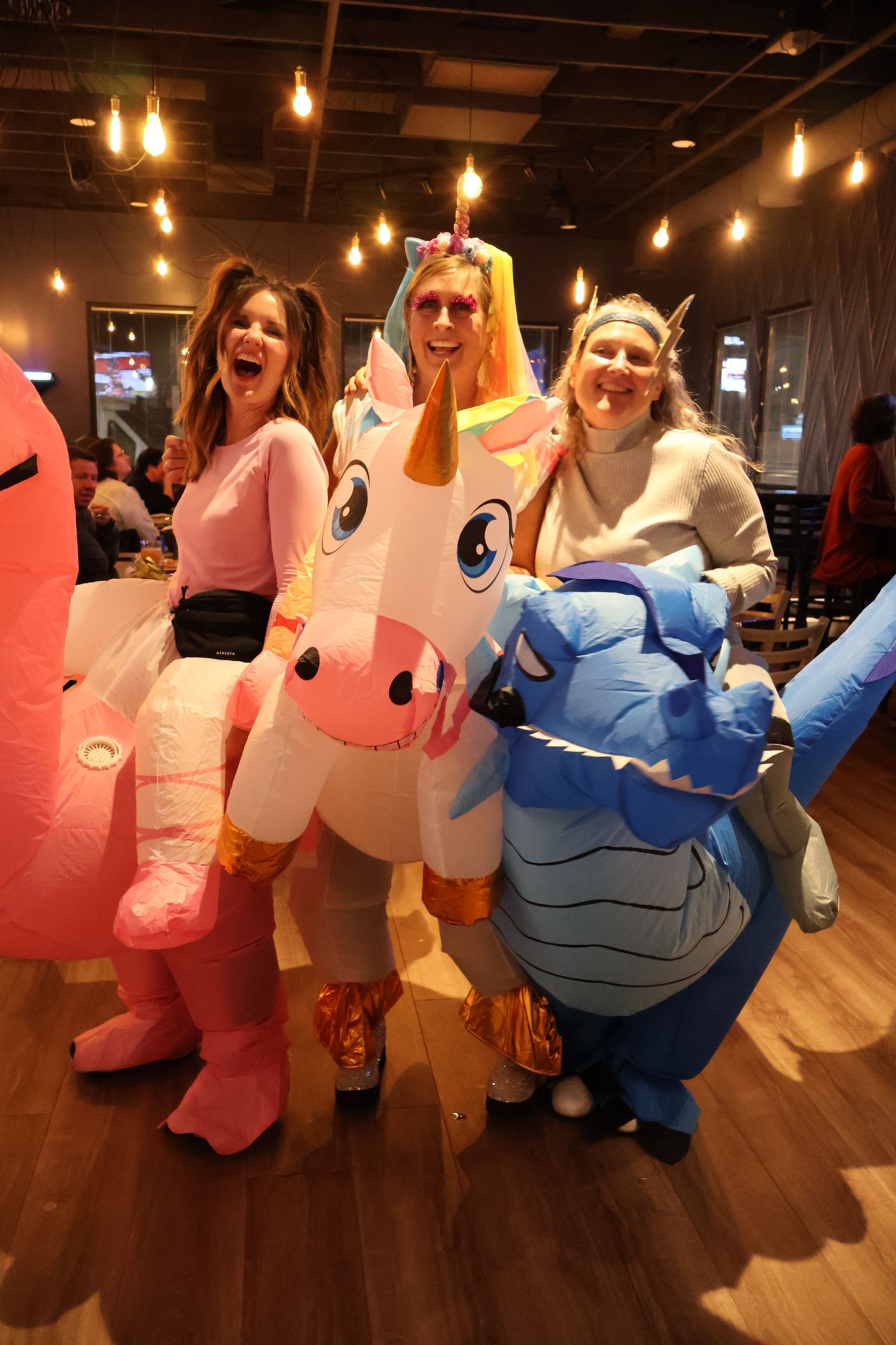 Three people in inflatable costumes posing for a photo. A flamingo, unicorn, and dragon.