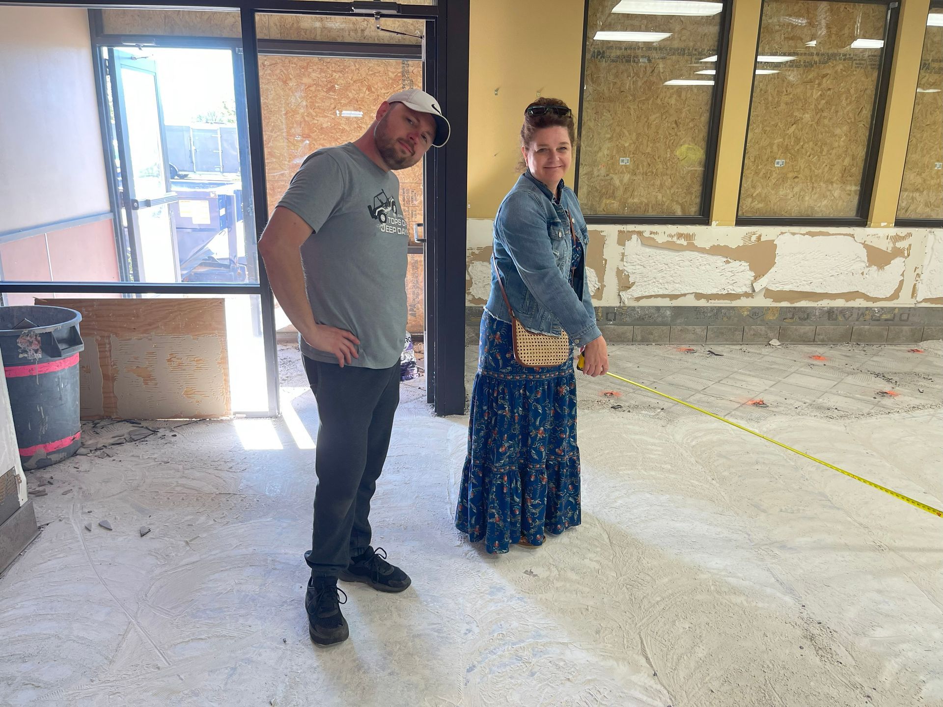 Man and woman in a room measuring with a tape. Room has exposed walls and floor.