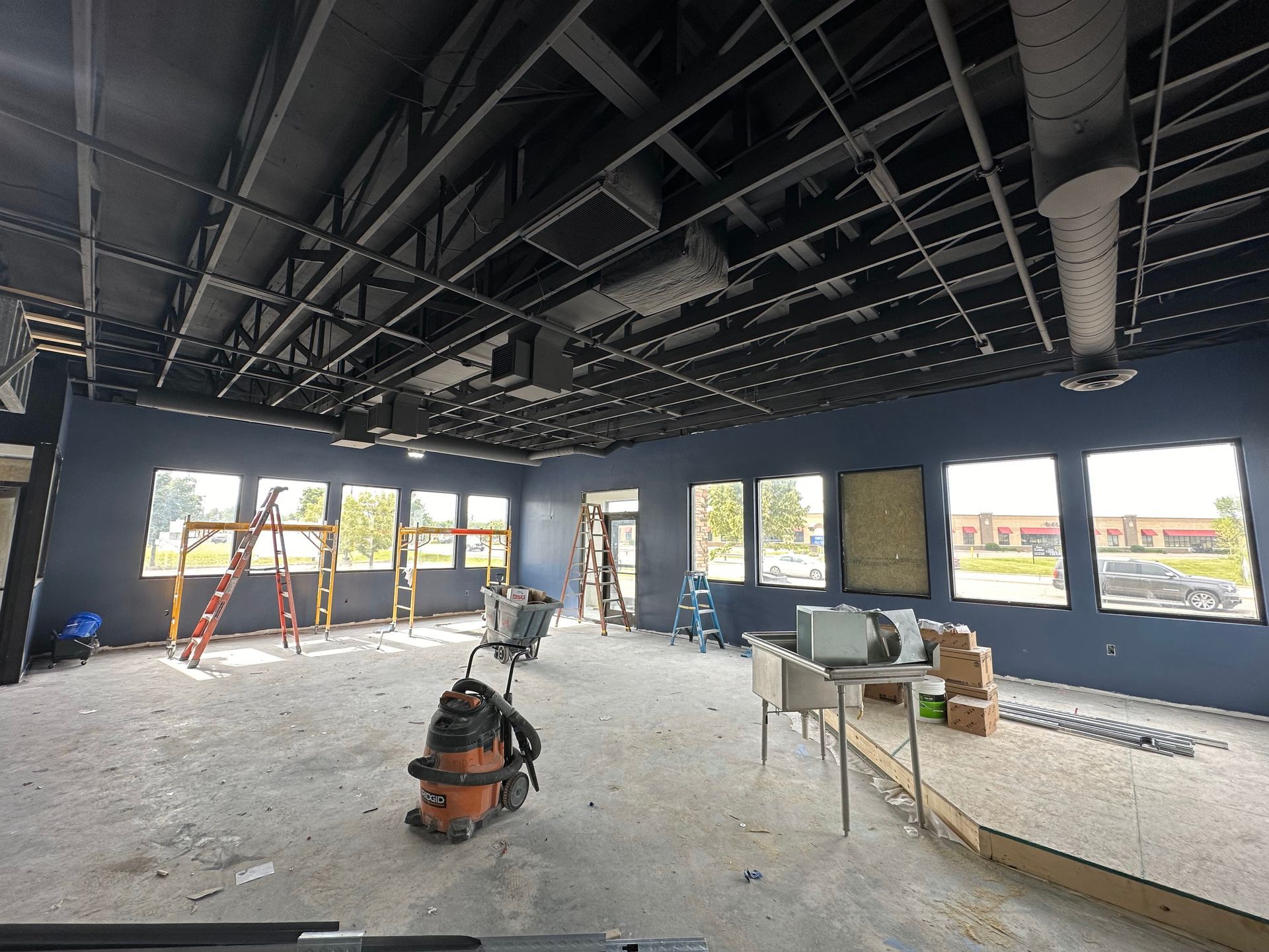 Interior construction site with black ceiling, dark blue walls, and multiple windows.