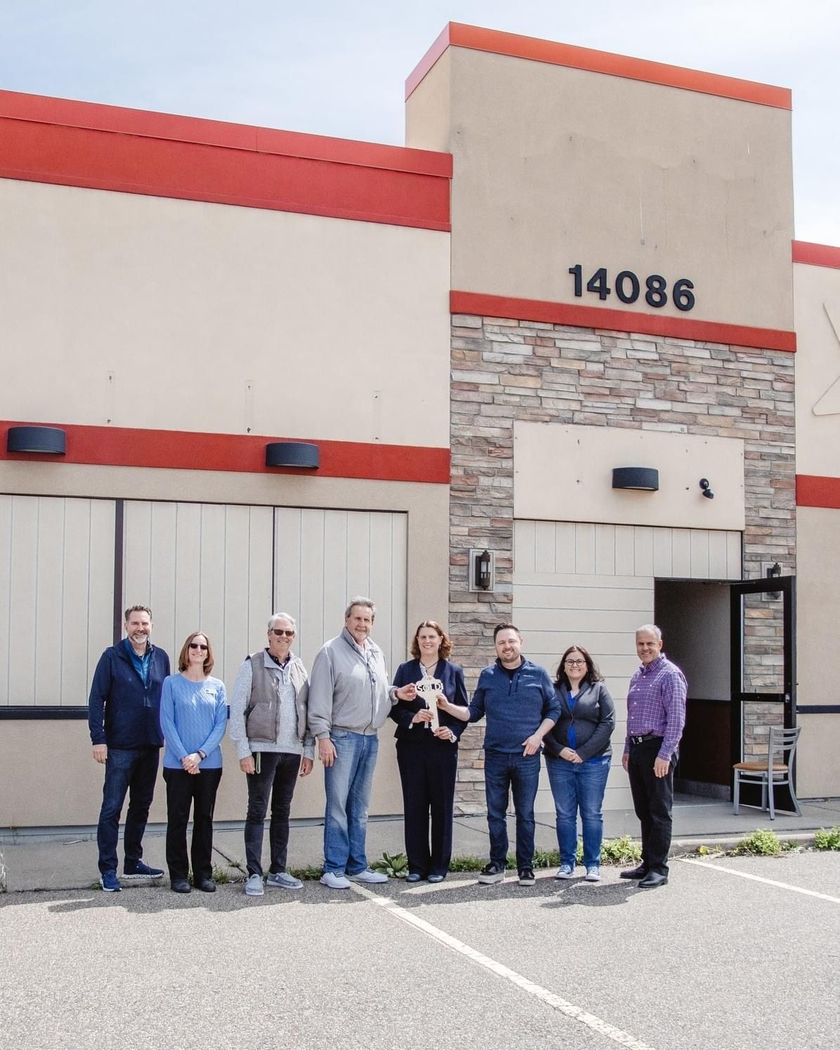 Group of people standing outside a commercial building with address 14086. Building is beige with red trim, stone facade at the entrance.