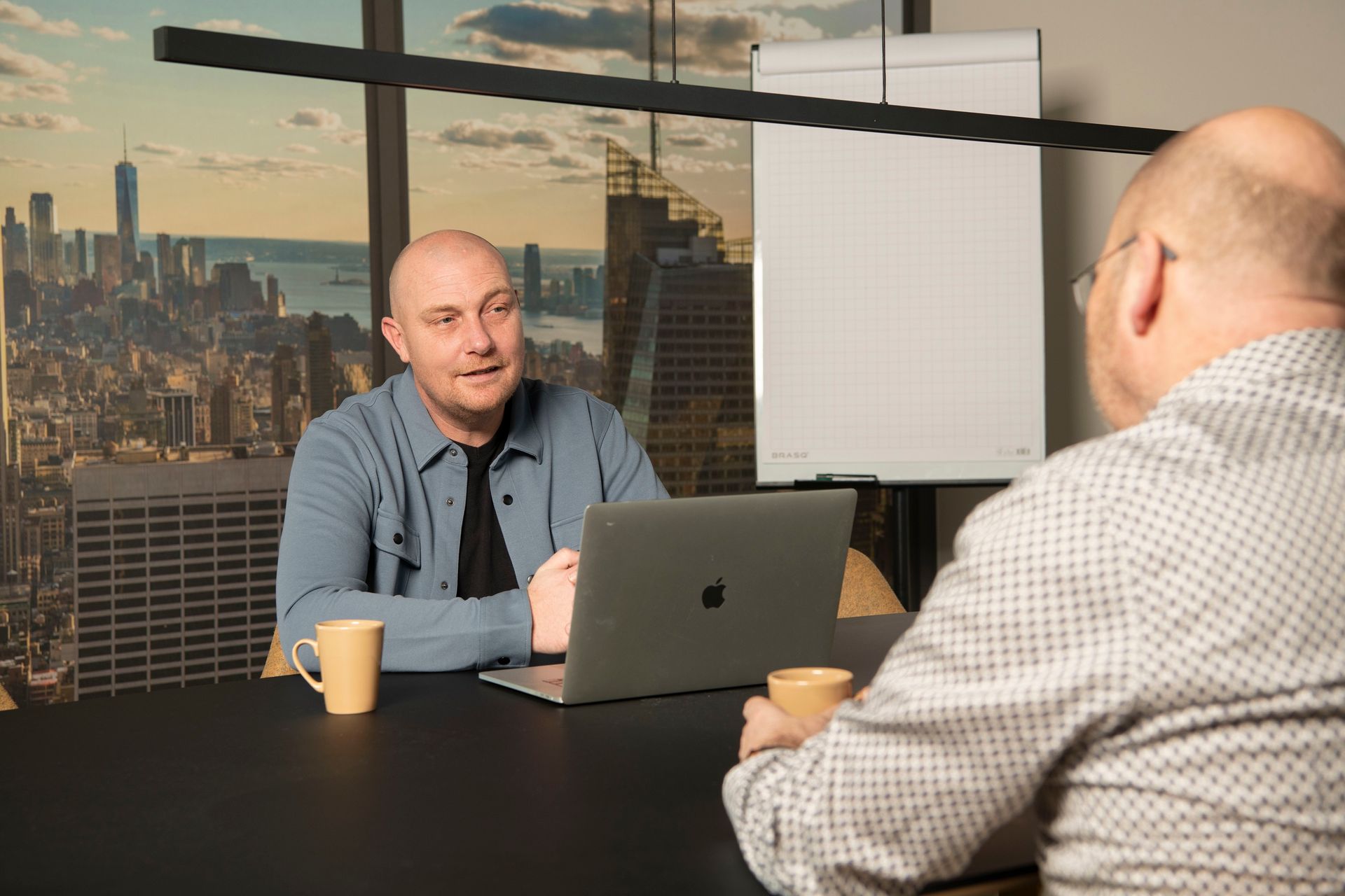 Two professionals in a modern office review information together on a tablet while sitting at a wooden desk.