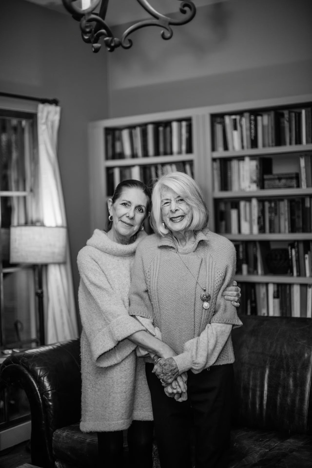 A black and white photo of two women standing next to each other in a living room.