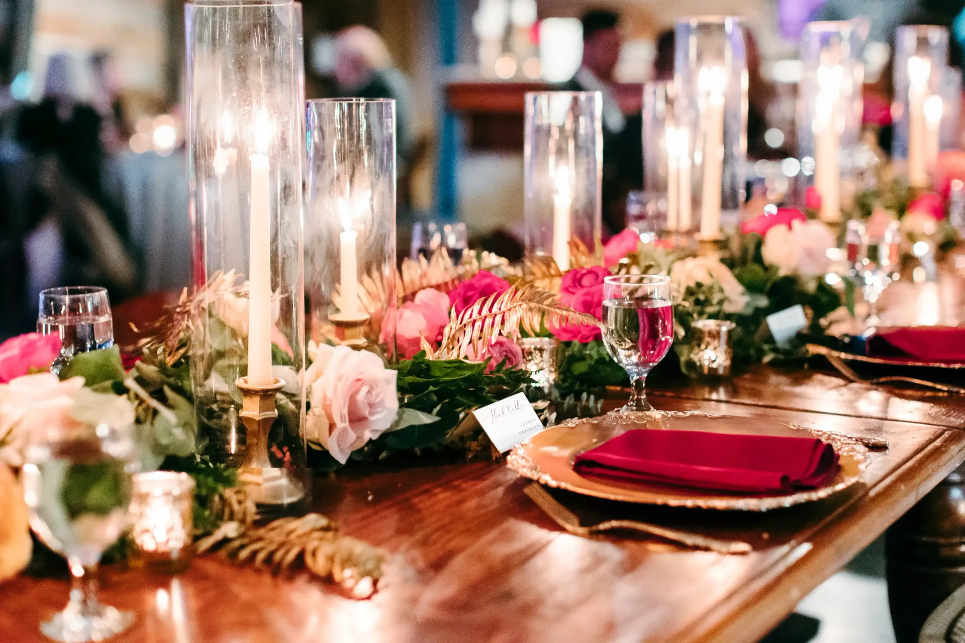 A table set for a wedding reception with plates , candles , and flowers.