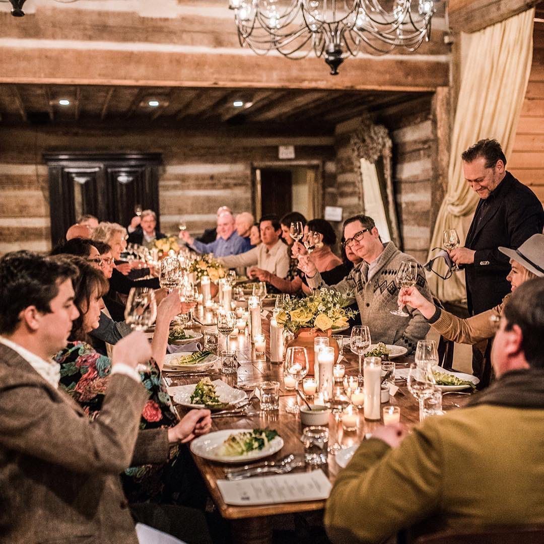 A group of people are sitting at a long table toasting with wine glasses.