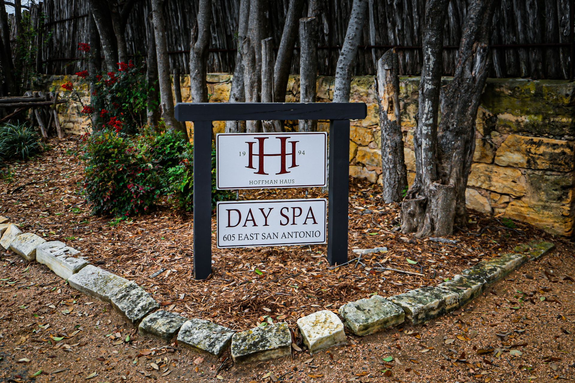 A sign for a day spa is surrounded by trees and rocks.