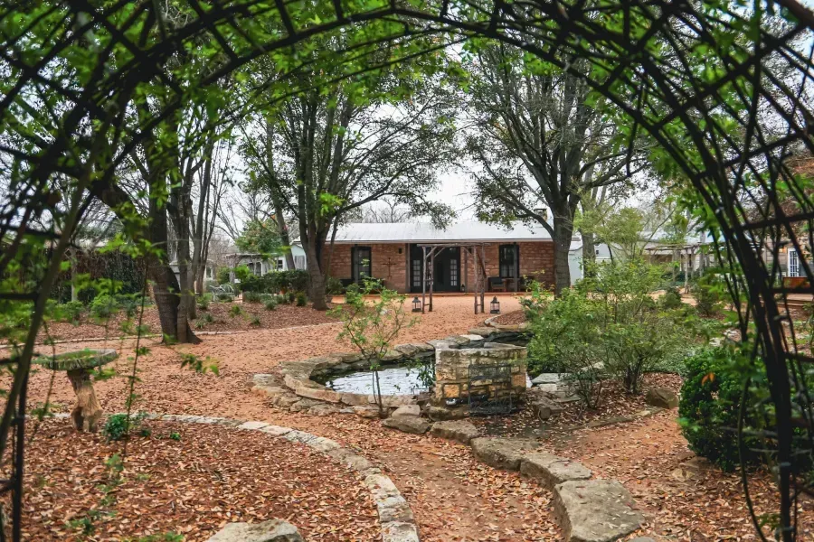 A house with a pond in front of it is surrounded by trees and leaves.
