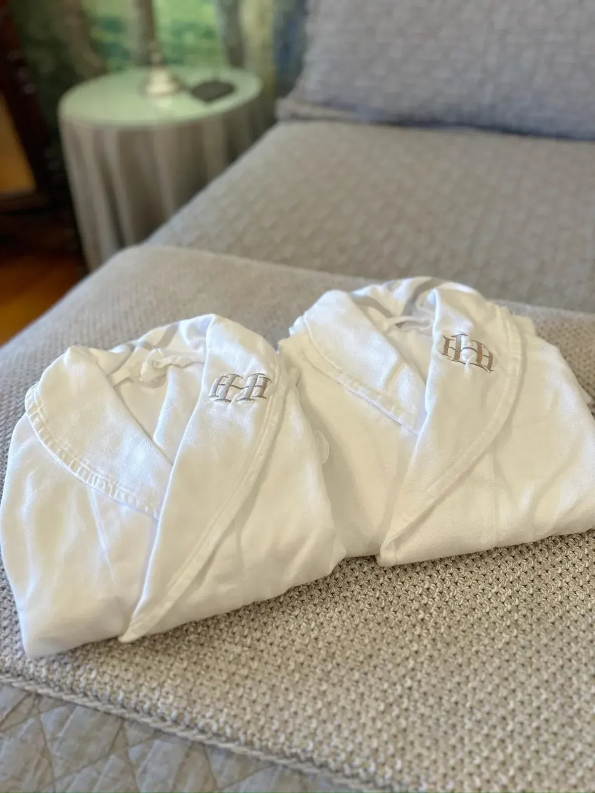 Two white robes with monograms on them are sitting on a bed.