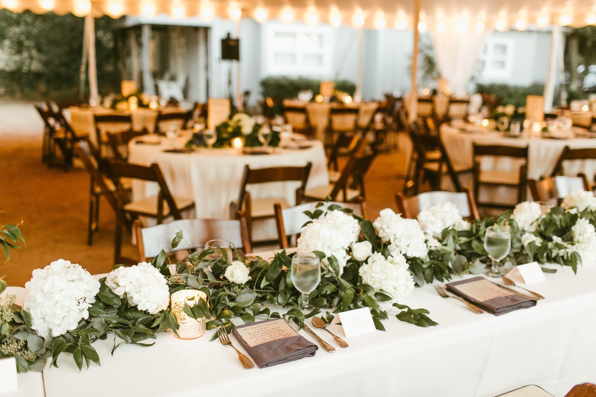 A wedding reception is being set up under a tent with tables and chairs.