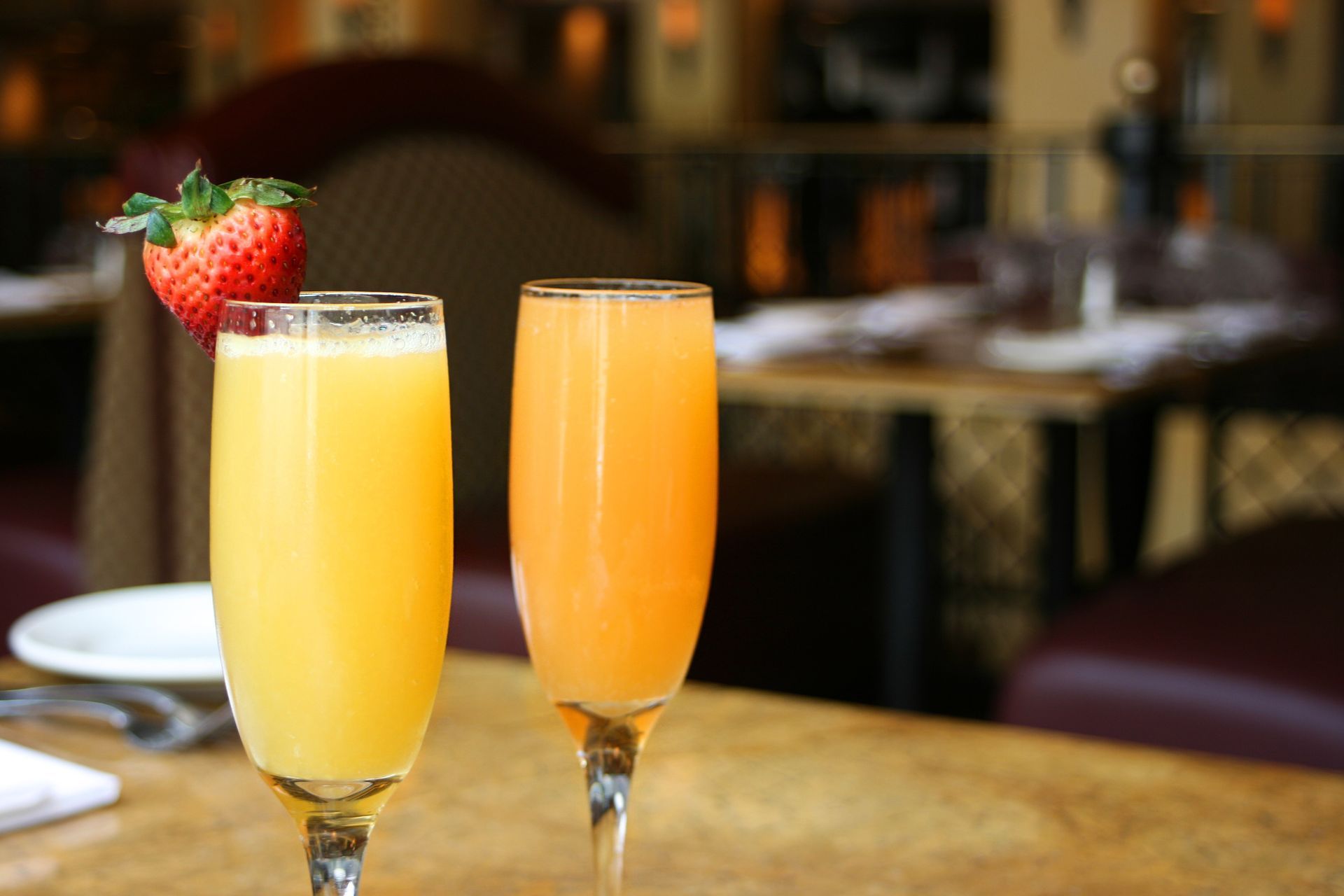 Two glasses of beverages with strawberries on top of them on a table.