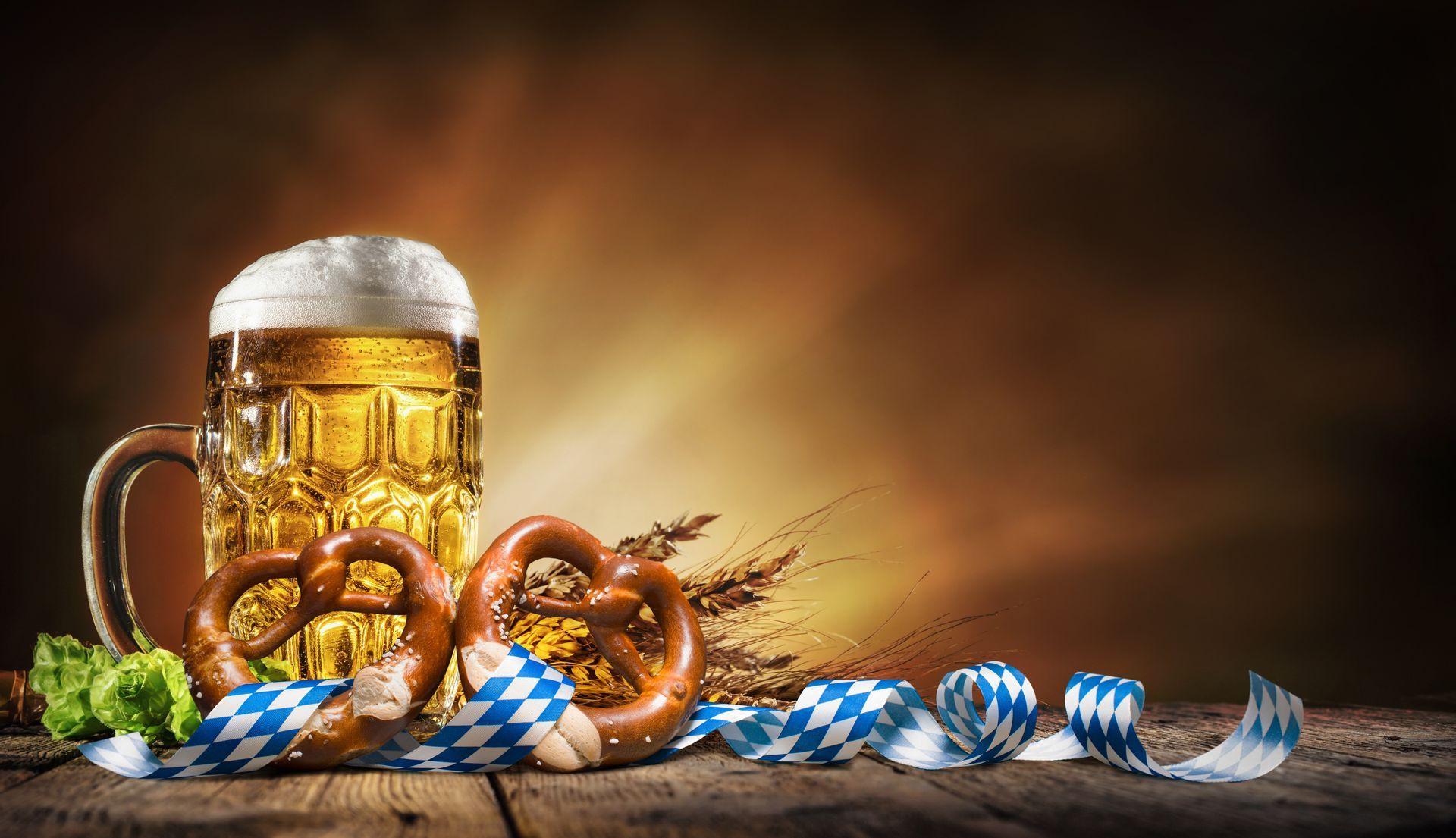 A mug of beer , pretzels , and wheat on a wooden table.