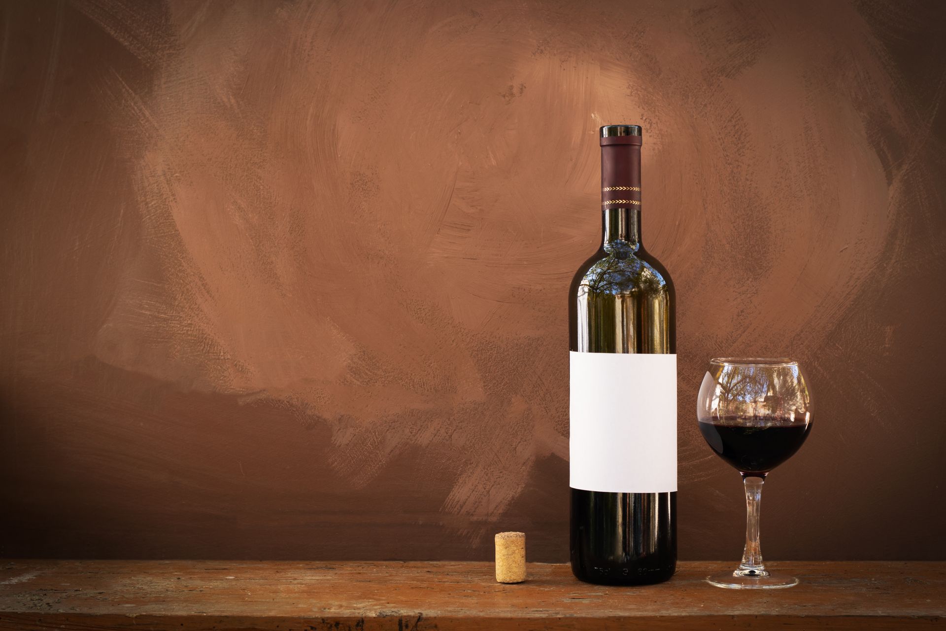 A bottle of wine and a glass of wine are on a wooden table.