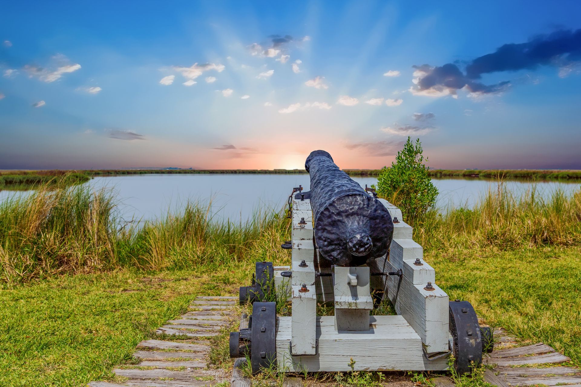 Cannon on a wooden carriage, facing lake, with sunset in the background.