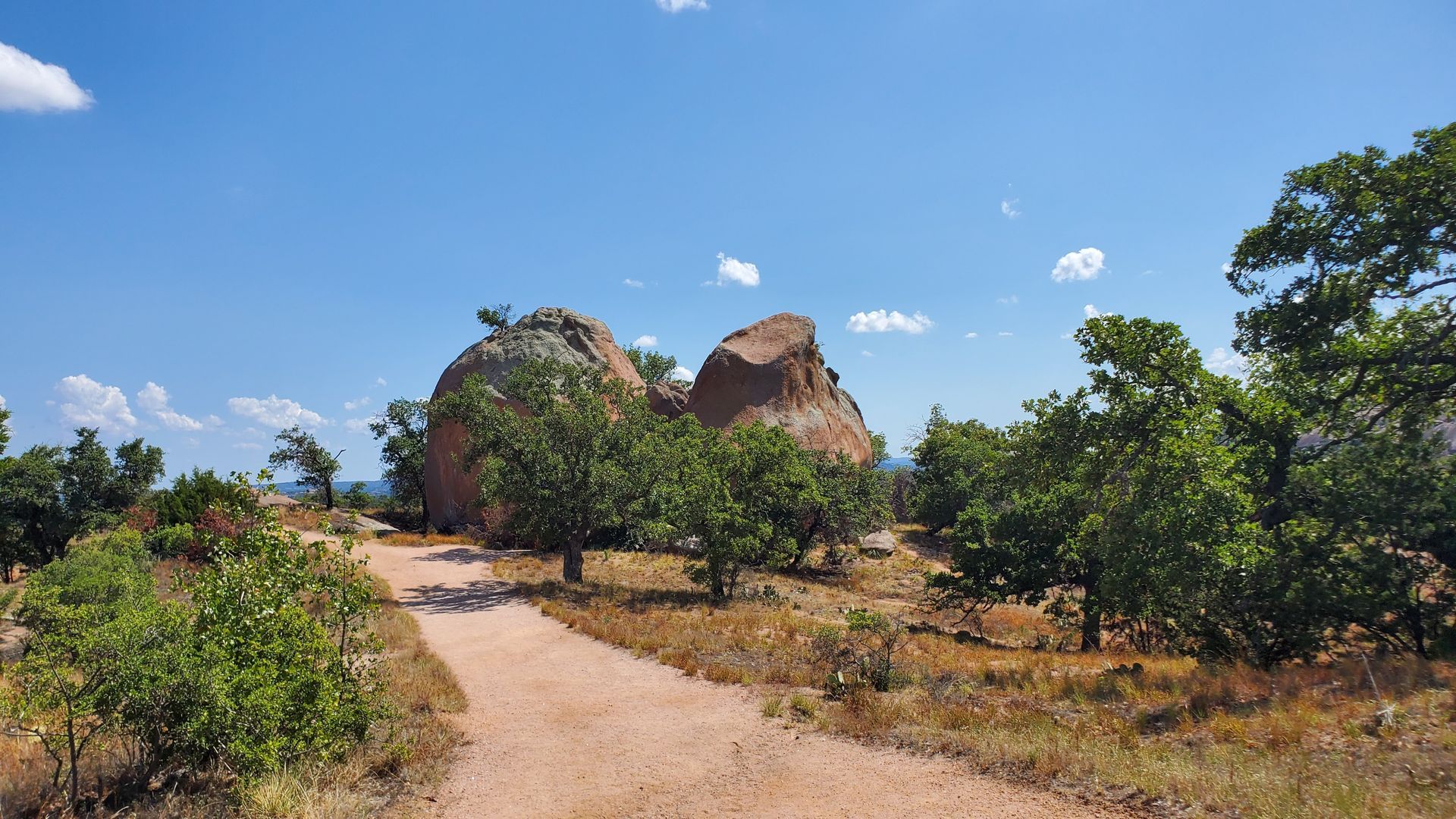 A dirt path leading to a large rock in the middle of a field.