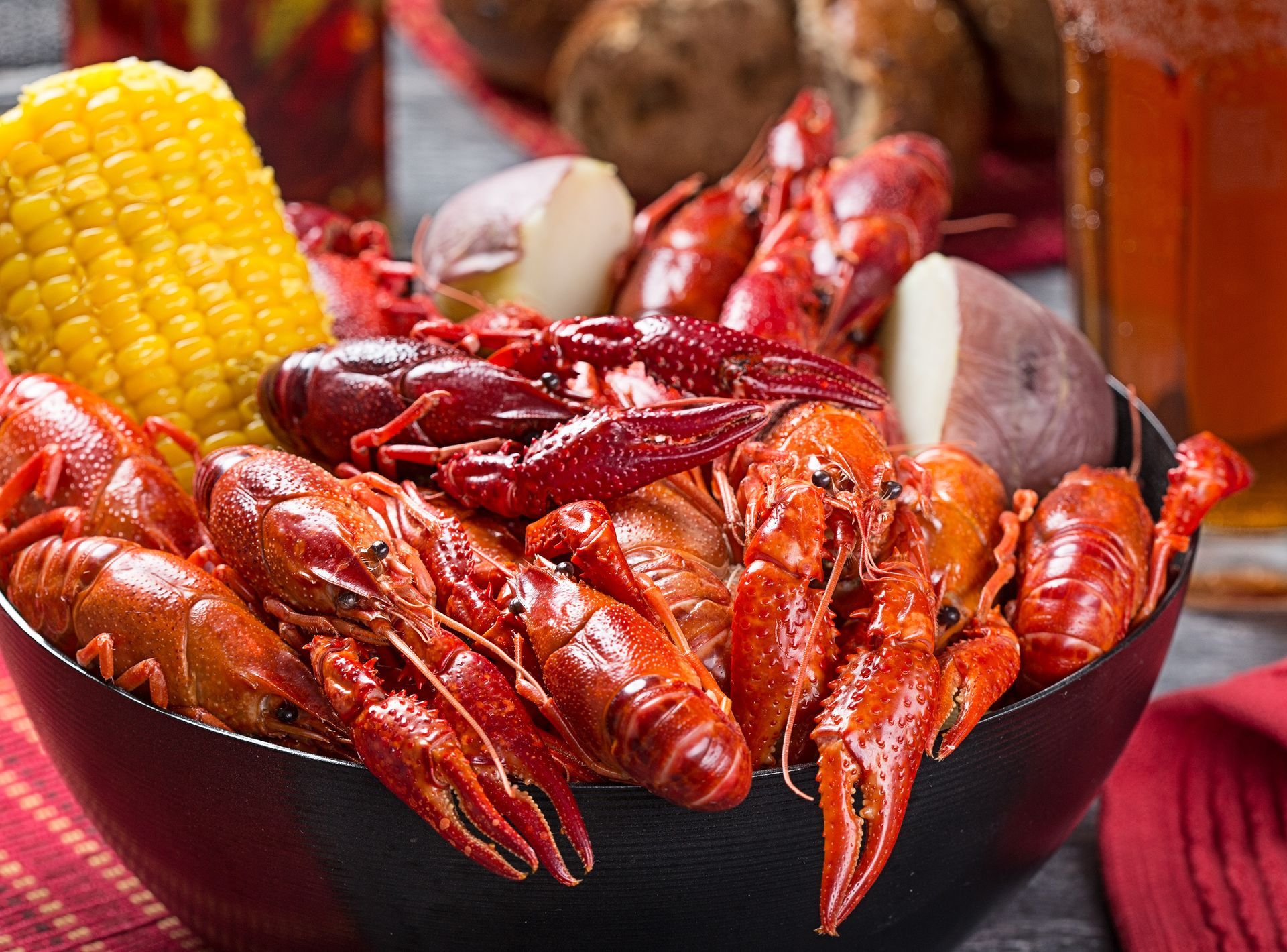 Bowl of cooked crawfish, corn on the cob, and potatoes. Red and orange hues, close up.