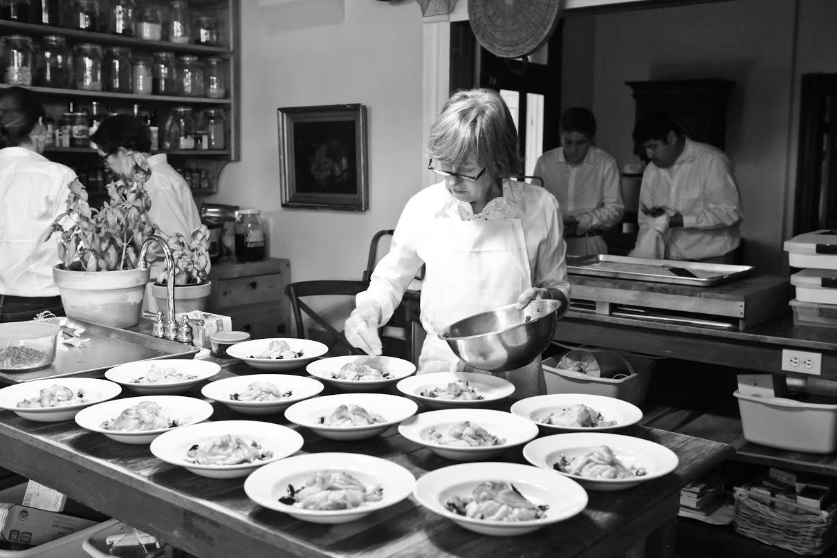 A black and white photo of a woman preparing food in a kitchen