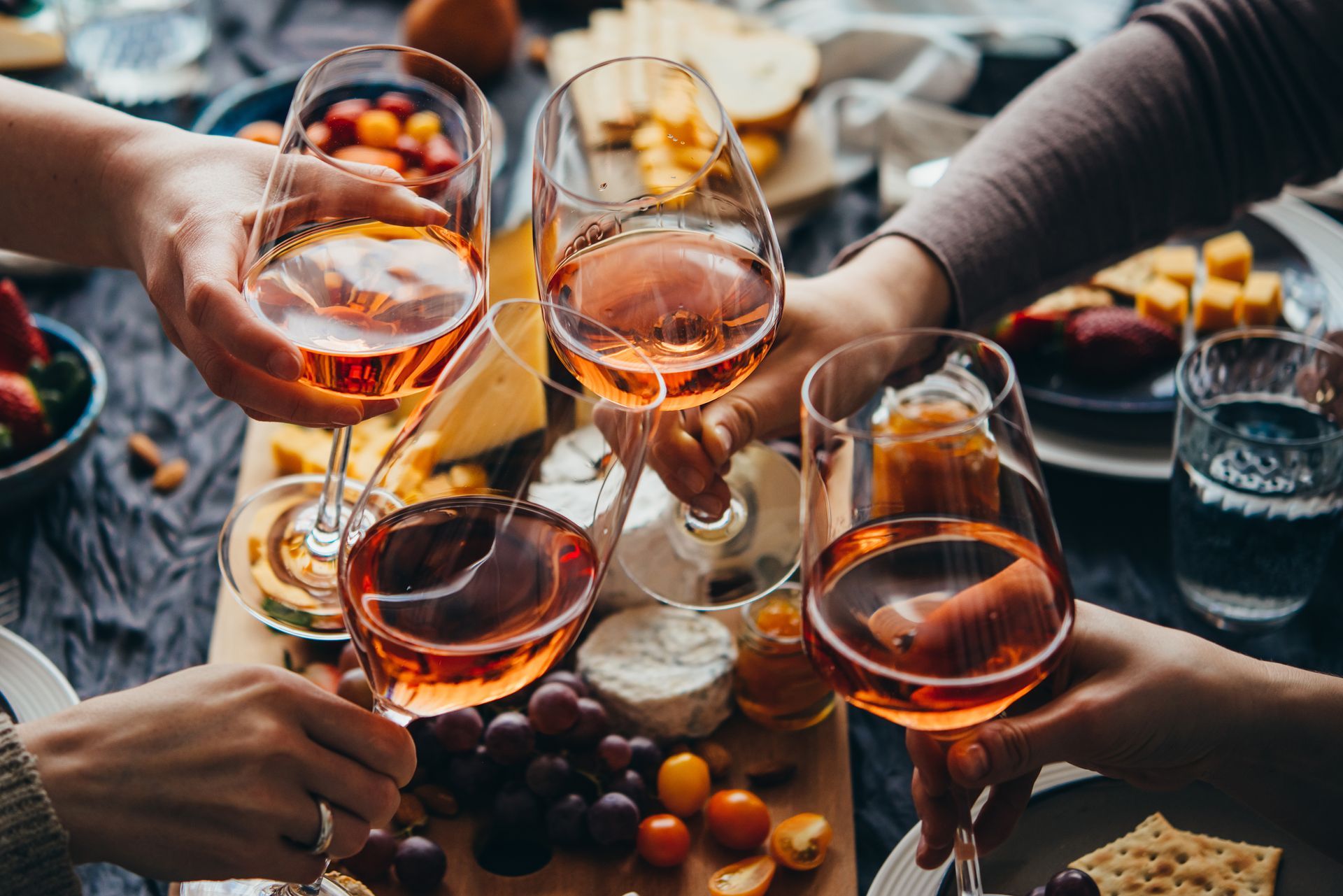 Hands toasting with rose wine glasses at a table with snacks.