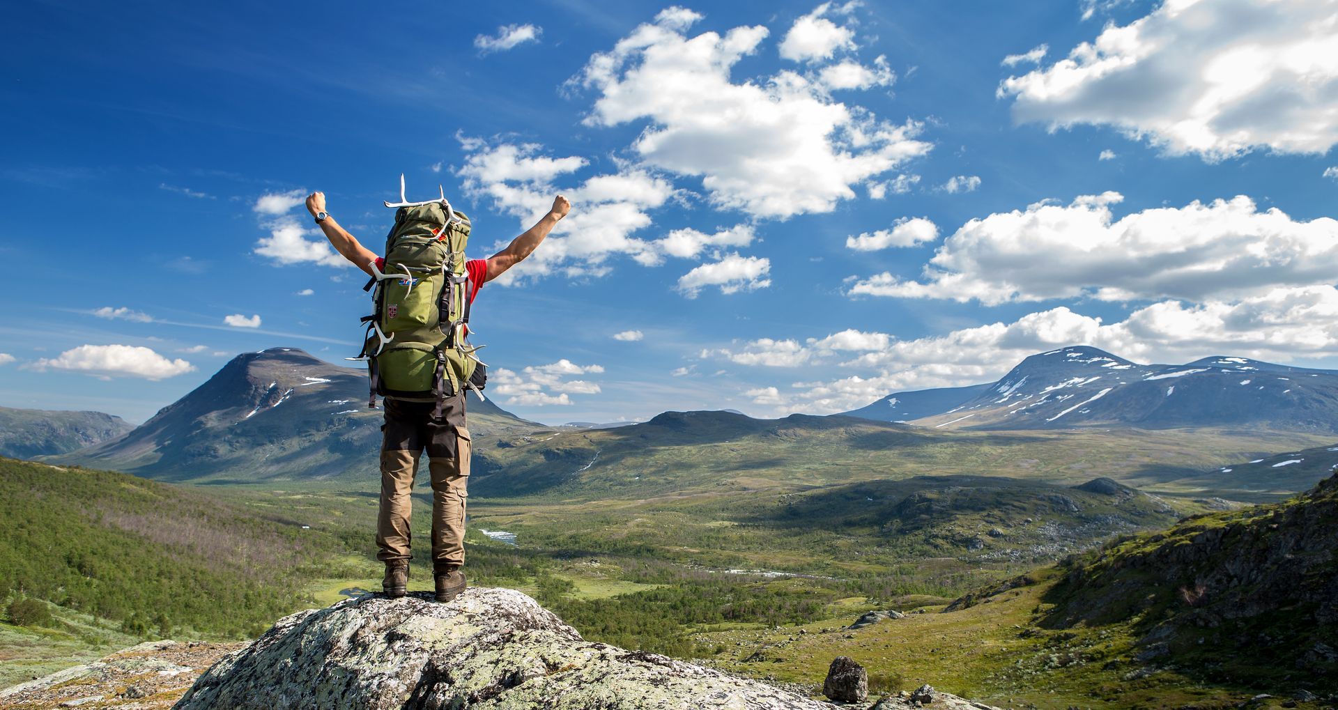 A person with a backpack is standing on top of a mountain with their arms in the air.