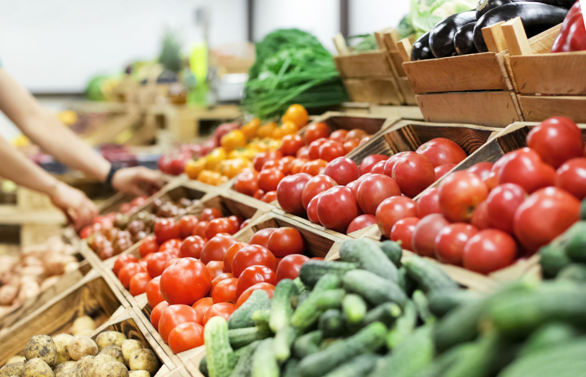 Person selecting tomatoes from a wooden produce display in a grocery store.