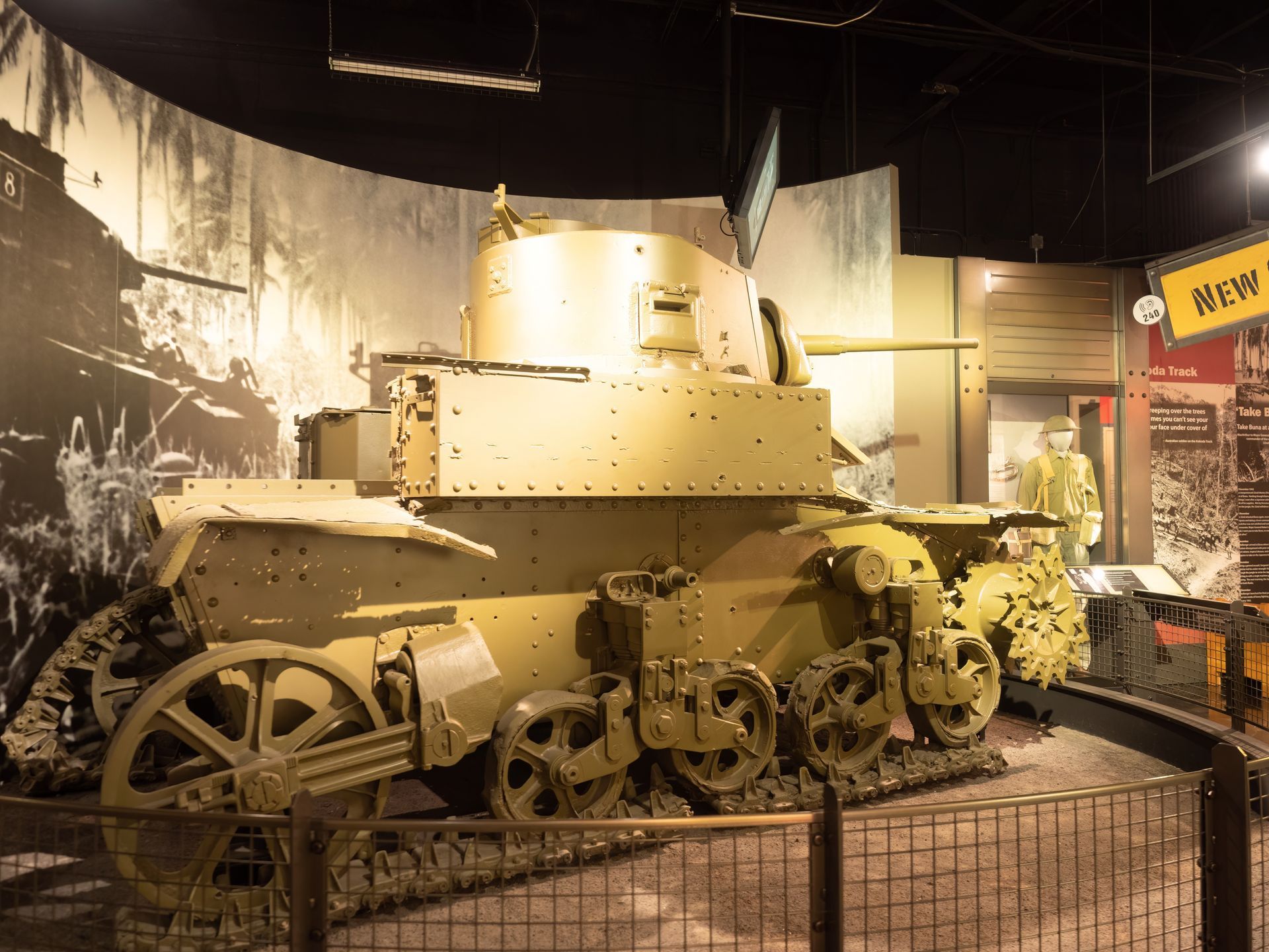An old tank is on display in a museum behind a fence.