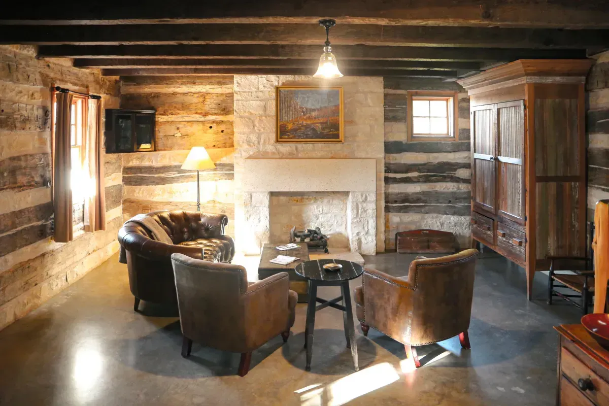 Cozy cabin interior with leather armchairs, fireplace, exposed beams, and a wooden wardrobe.