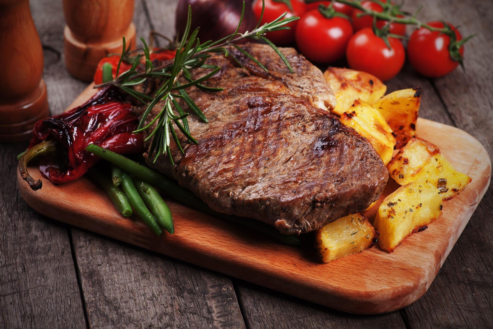 A steak with potatoes and green beans on a wooden cutting board.