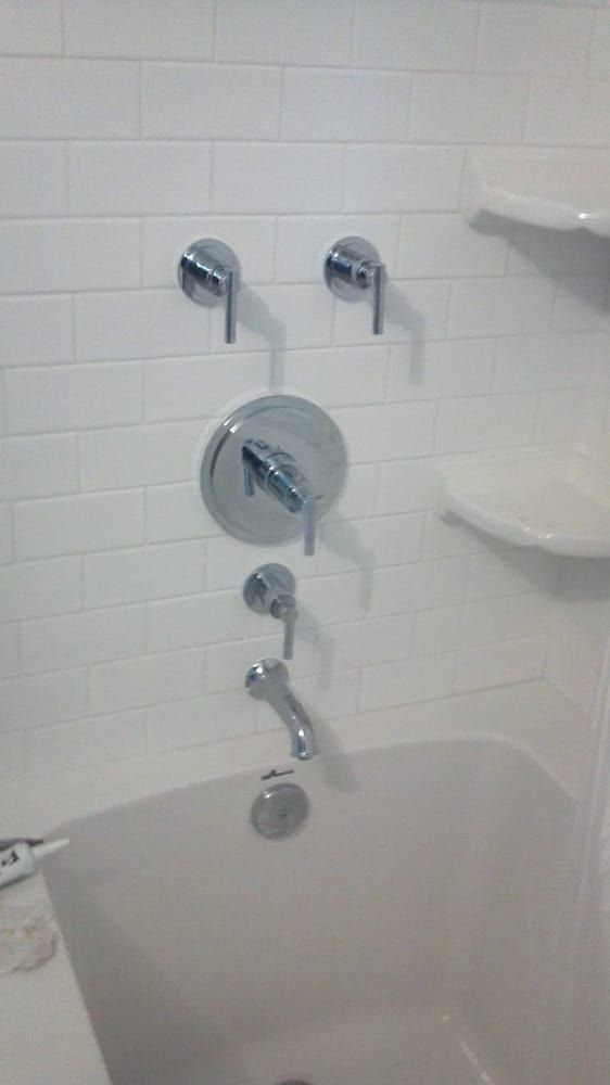 a bathtub with chrome shower faucets on a white tiled wall .