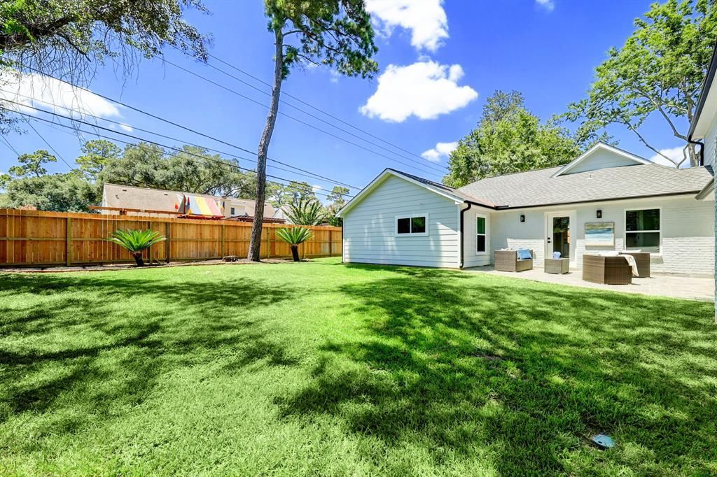 The backyard of a house with a large lawn and a wooden fence.