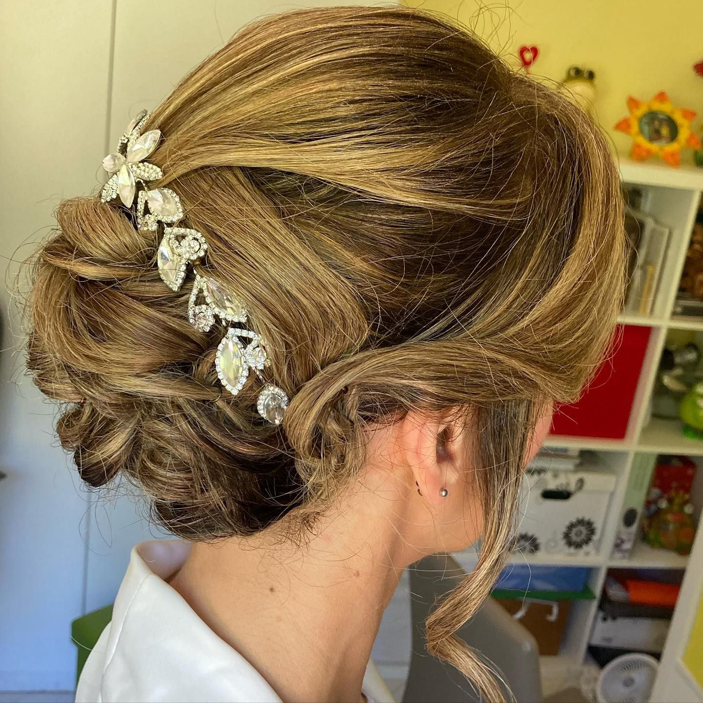 Donna con elaborata acconciatura raccolta, adornata con una parrucca gioiello, davanti a uno scaffale.