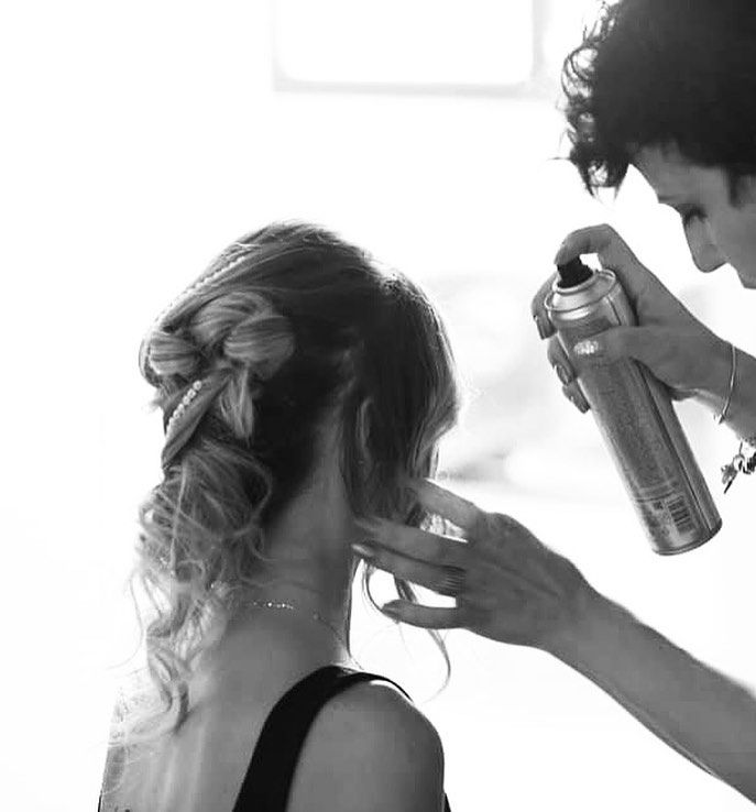 Capelli di una donna che si sistemano con la lacca. Una mano regge la bomboletta, lasciando visibile la schiena della donna.