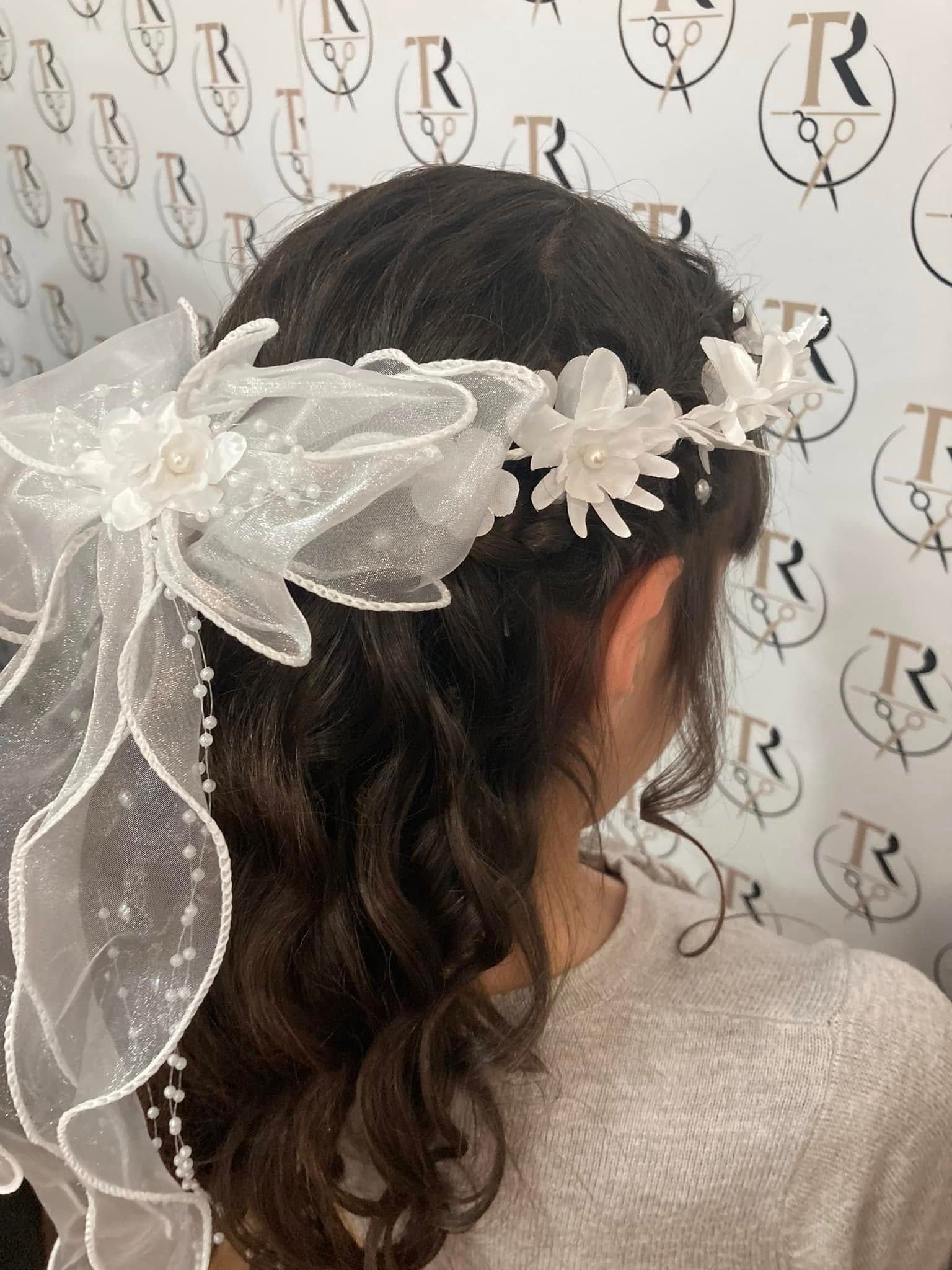 Ragazza con i capelli castani ricci che indossa una corona di fiori bianchi e un velo.