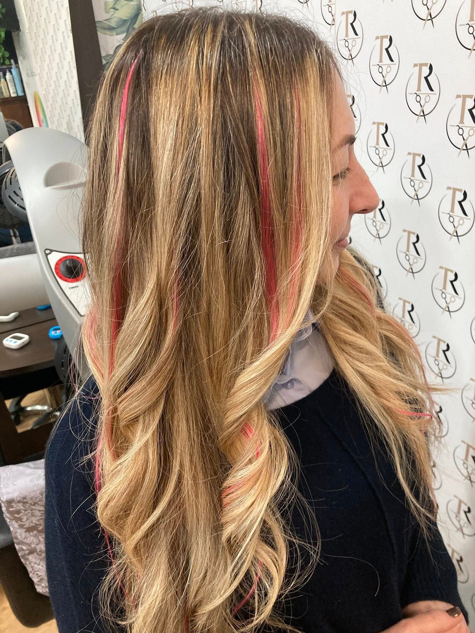 Donna con lunghi capelli biondi ondulati con ciocche rosa, ricoperti di glitter. In un salone di bellezza.