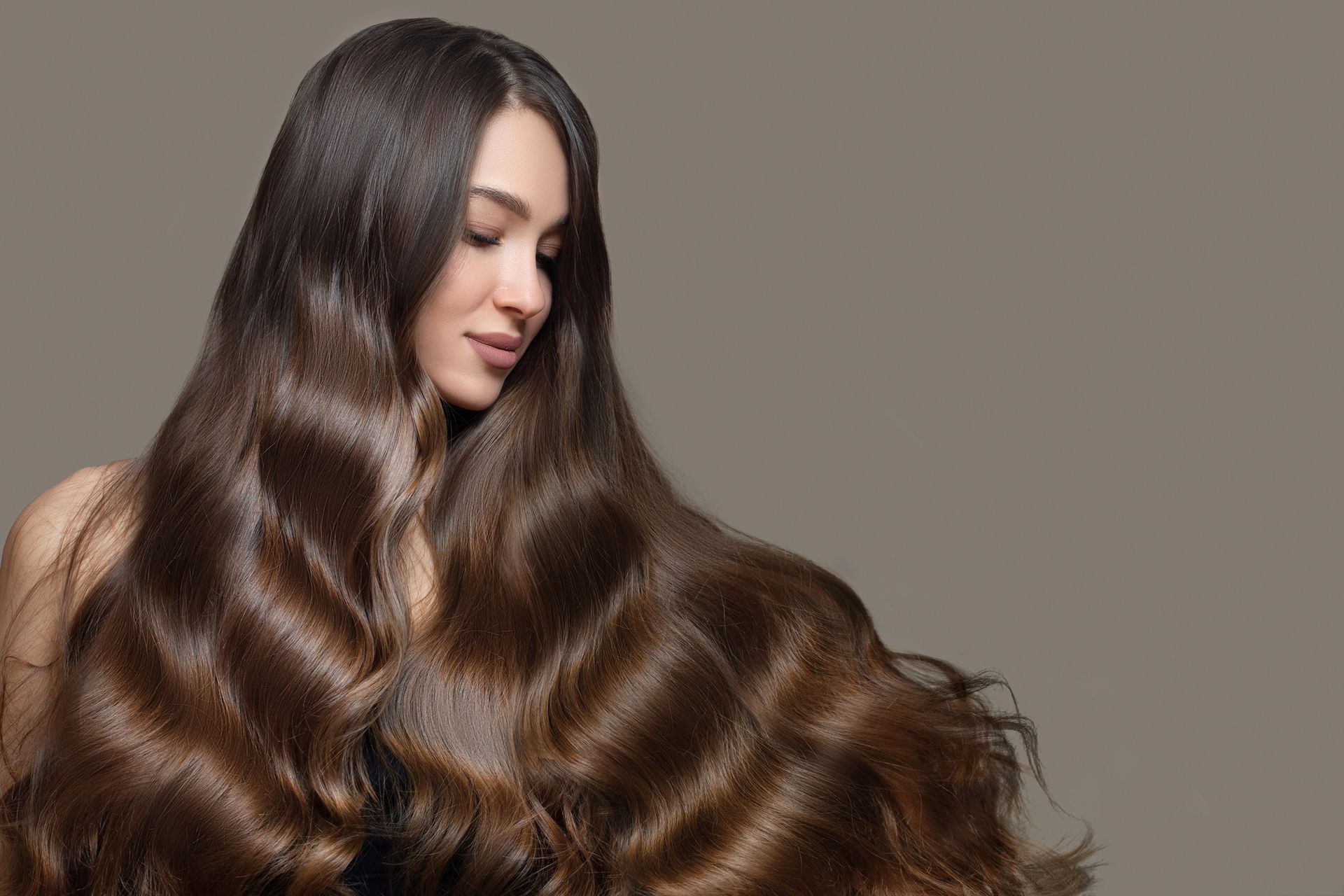 Donna con lunghi capelli castani e lucenti, occhi chiusi, sorridente, su uno sfondo neutro.