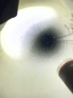 Looking down a dark hole, illuminated by a flashlight. Ice and snow surround the opening.