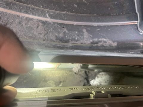 Close-up of a dryer showing a built-up lint and the insert filter opening. A hand holds a flashlight.