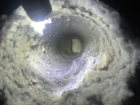 Inside a white, dusty vent, looking down towards a rectangular opening.