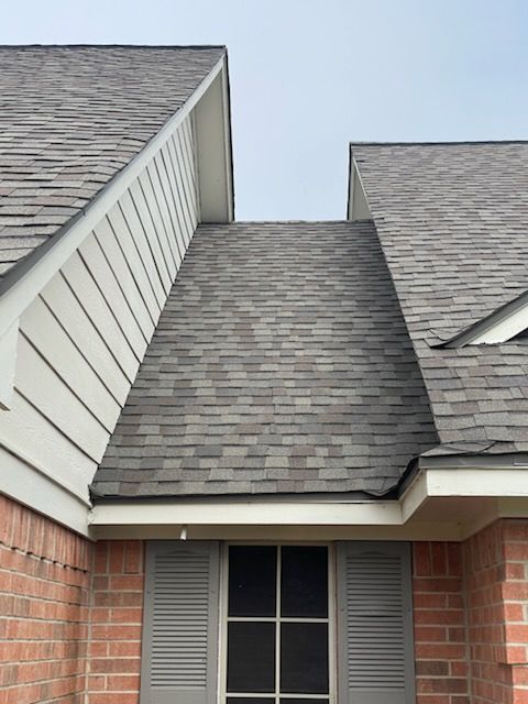 Gray shingled roof with a brick exterior. White trim around the window and roof edges.