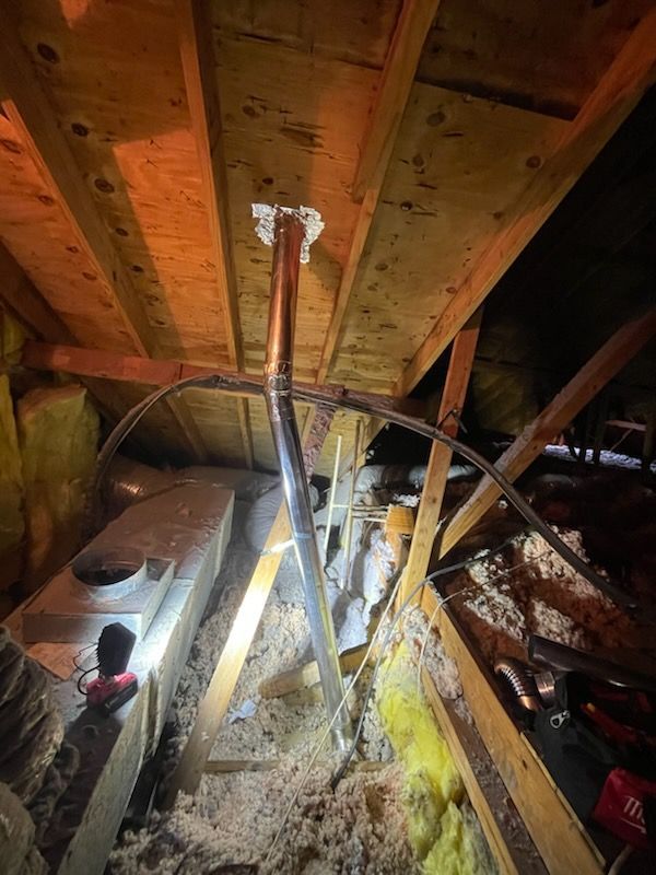 An attic with bent metal pipe extending from the ceiling. Insulation and wooden beams are visible.