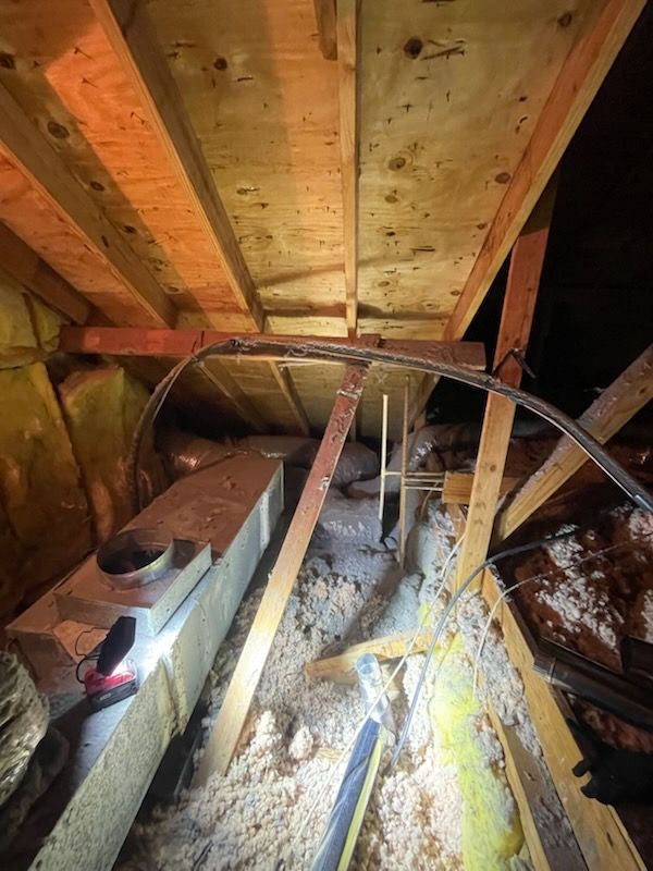 Attic view: Ductwork, insulation, and wiring among wooden beams and boards.